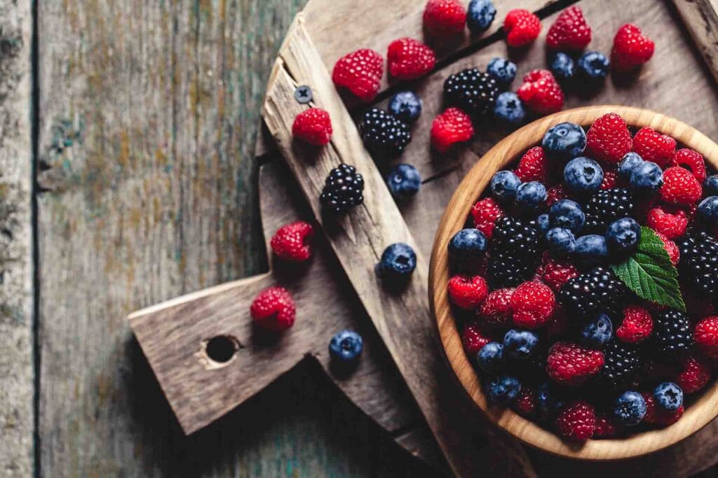 Assorted fresh berries in a wooden bowl and on a rustic wooden board, symbolizing natural nourishment and healthy choices.